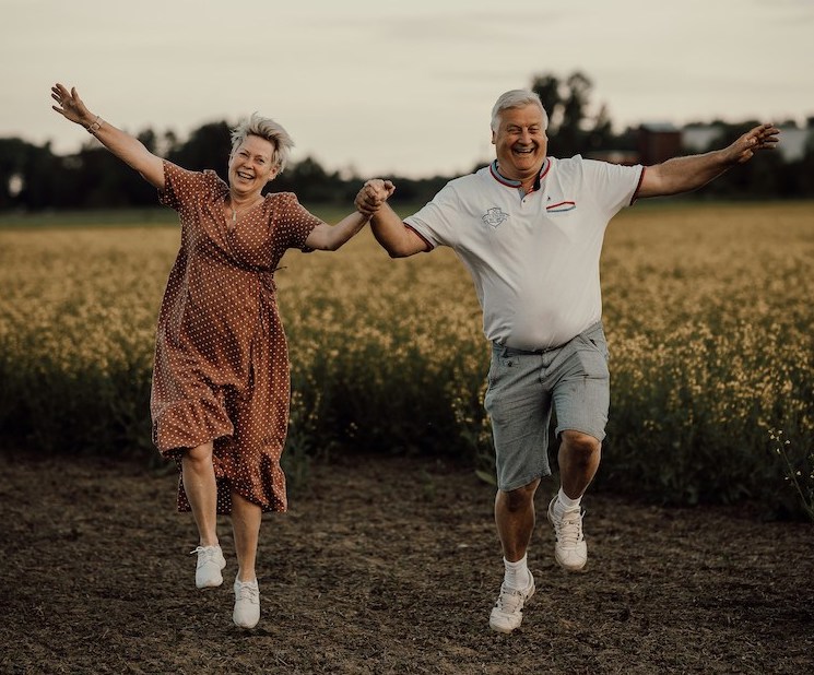 Älteres Paar springt Hand in Hand fröhlich in die Luft