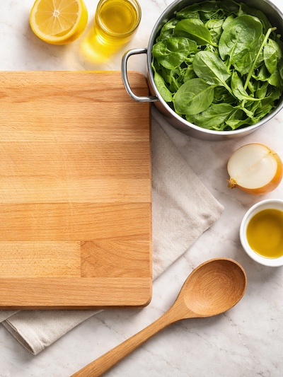 Schneidebrett mit Spinat, Öl, Zitrone und Holzlöffel